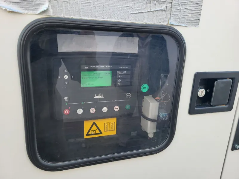 Steuerung von Deep Sea Electronics hinter dem Sichtfenster in der Generatortür: Auf dem Display steht „Generator at Rest“, darunter die Tasten für Start und Stopp.